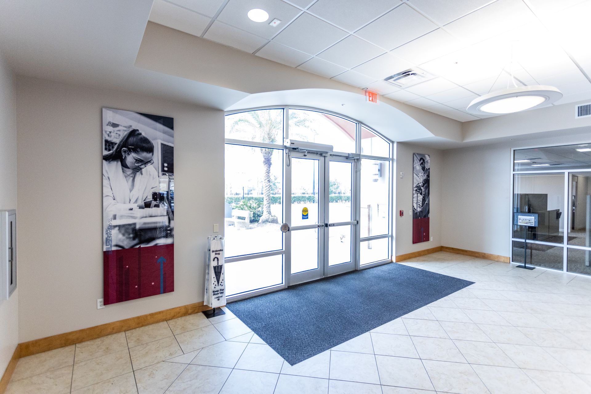 Interior view of the Florida Tech office entrance. Features large glass doors, tile floor, and wall art depicting scientific activities, creating a welcoming atmosphere